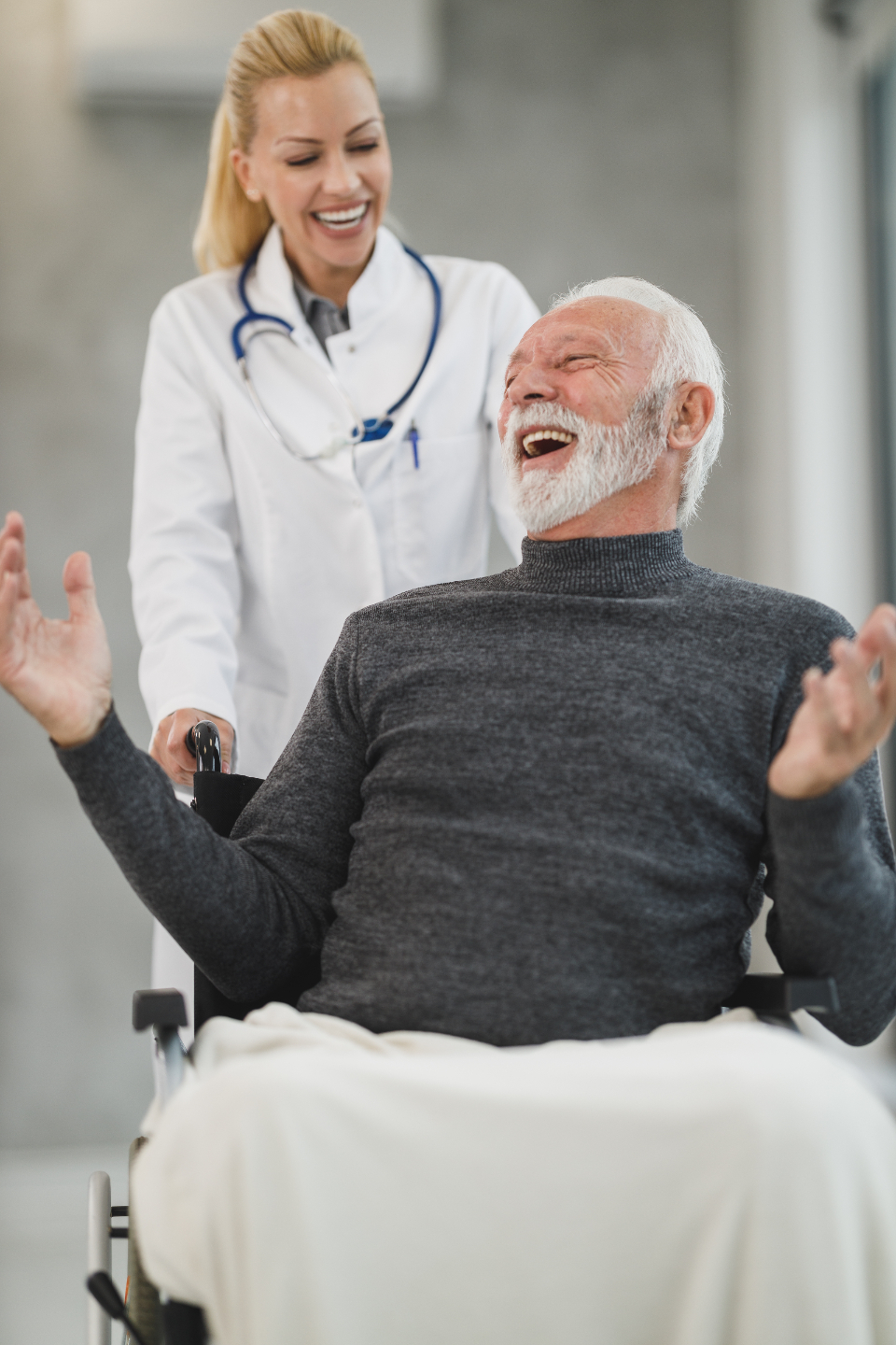 A joyful caregiver laughing together with a happy client in a wheelchair